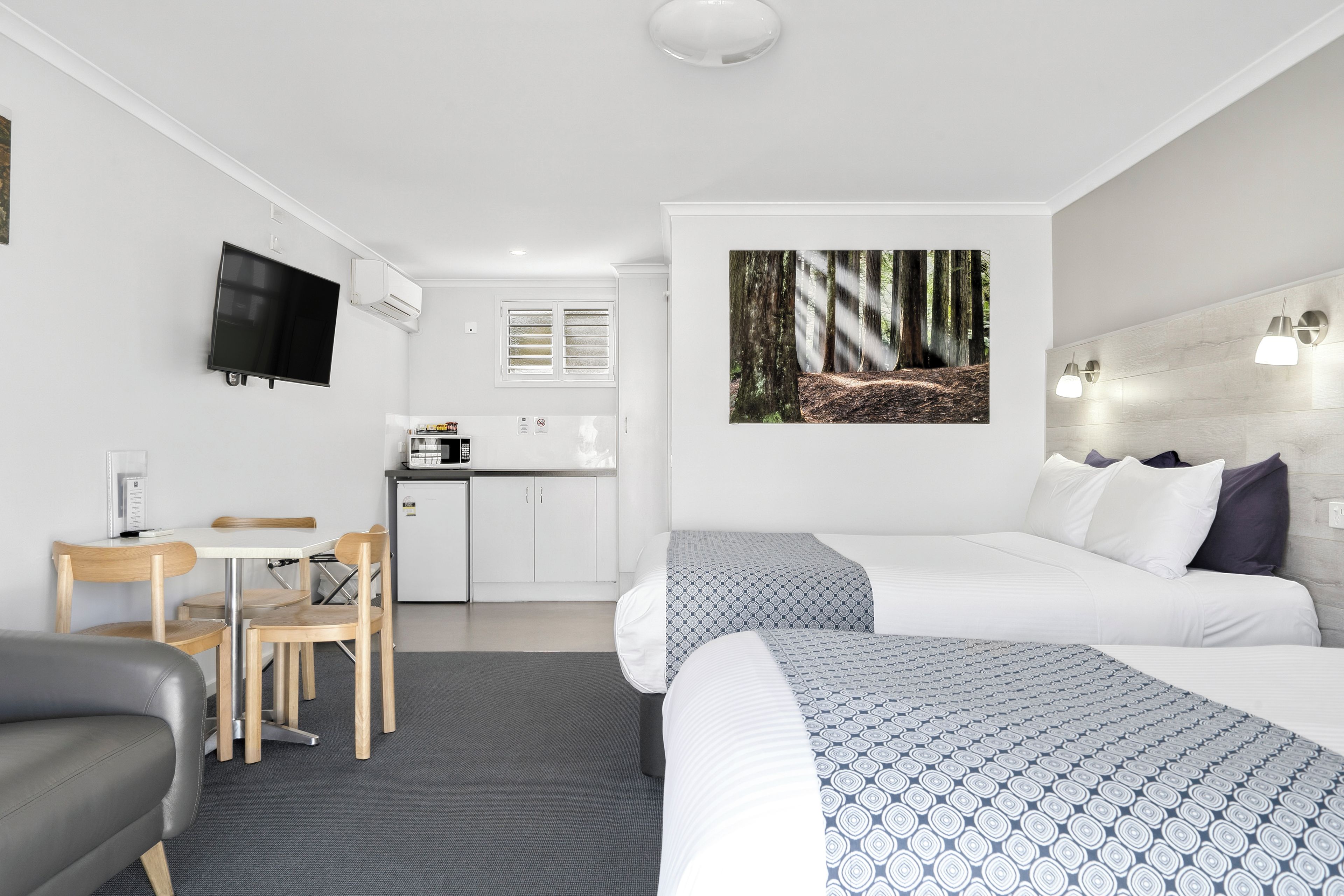 A hotel room with a bed, a desk, a chair, a television, and a kitchen area.