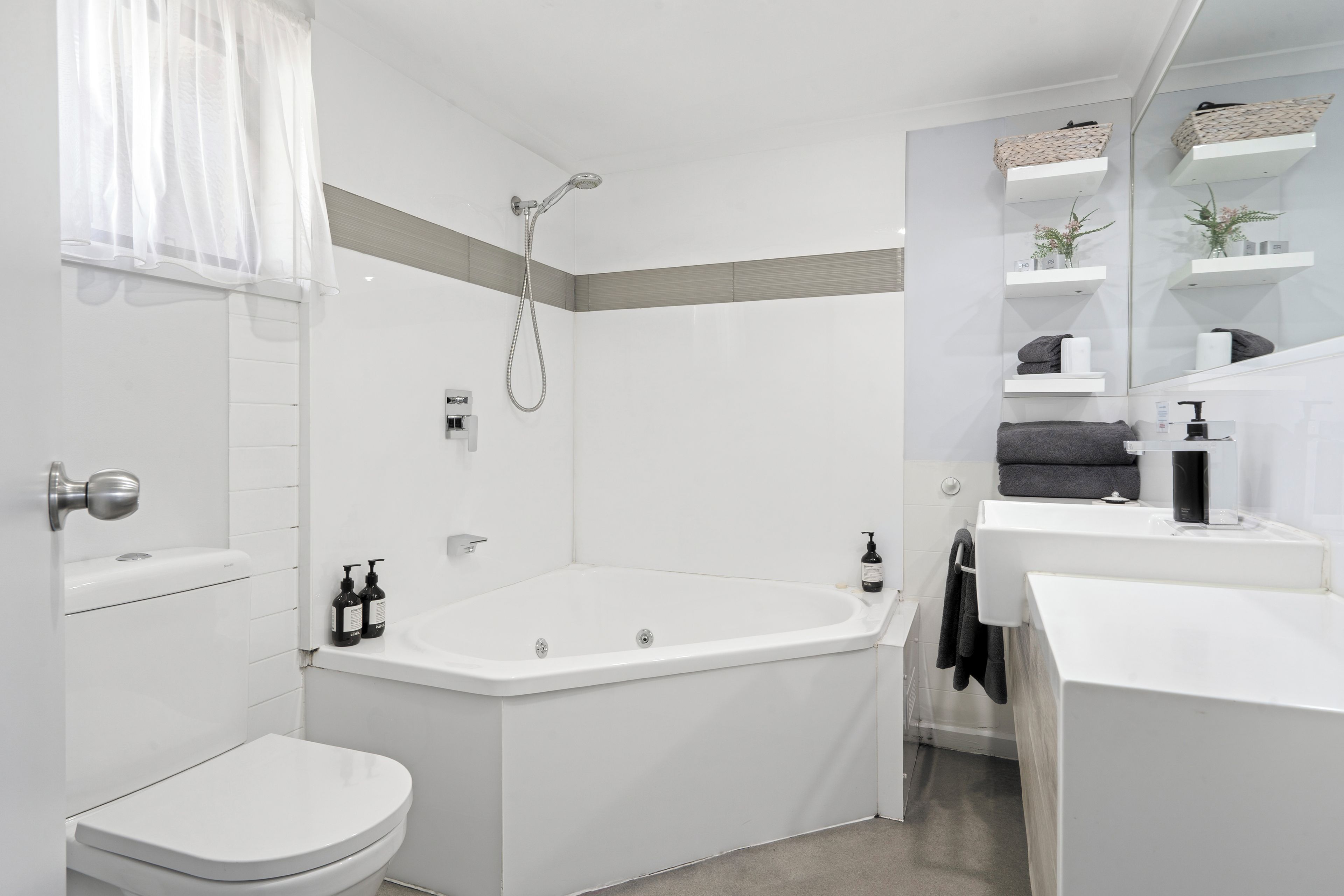 Un baño moderno con inodoro, bañera y ducha. Hay repisas con artículos de aseo personal y un perchero para toallas.