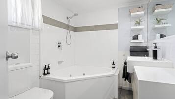 Un baño moderno con inodoro, bañera y ducha. Hay repisas con artículos de aseo personal y un perchero para toallas.