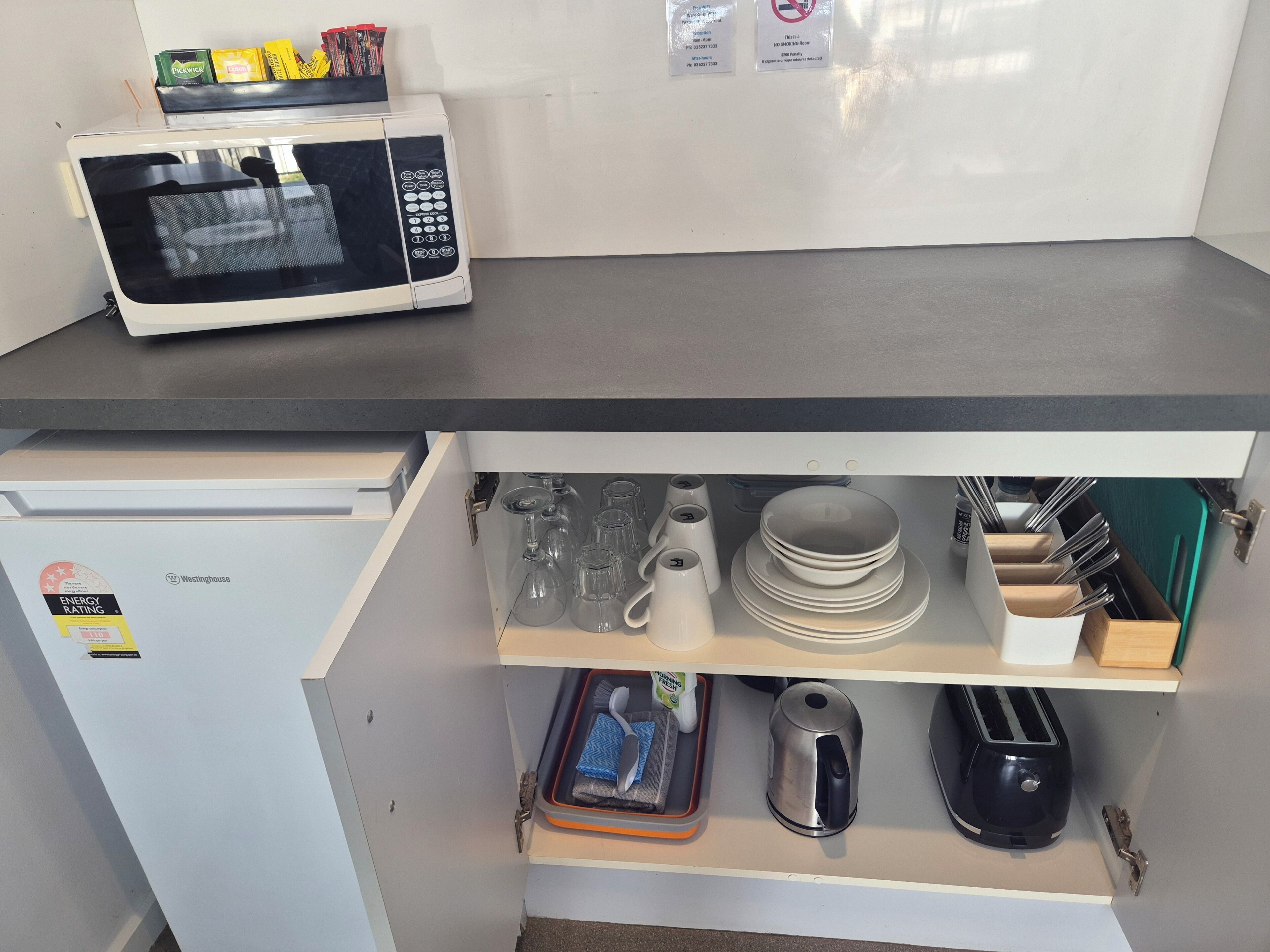 Een keuken met een magnetron op het aanrecht, een koelkast en een lade met keukengerei en servies.