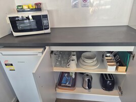 Una cocina con un microondas en la encimera, un refrigerador y un cajón con utensilios y vajilla.