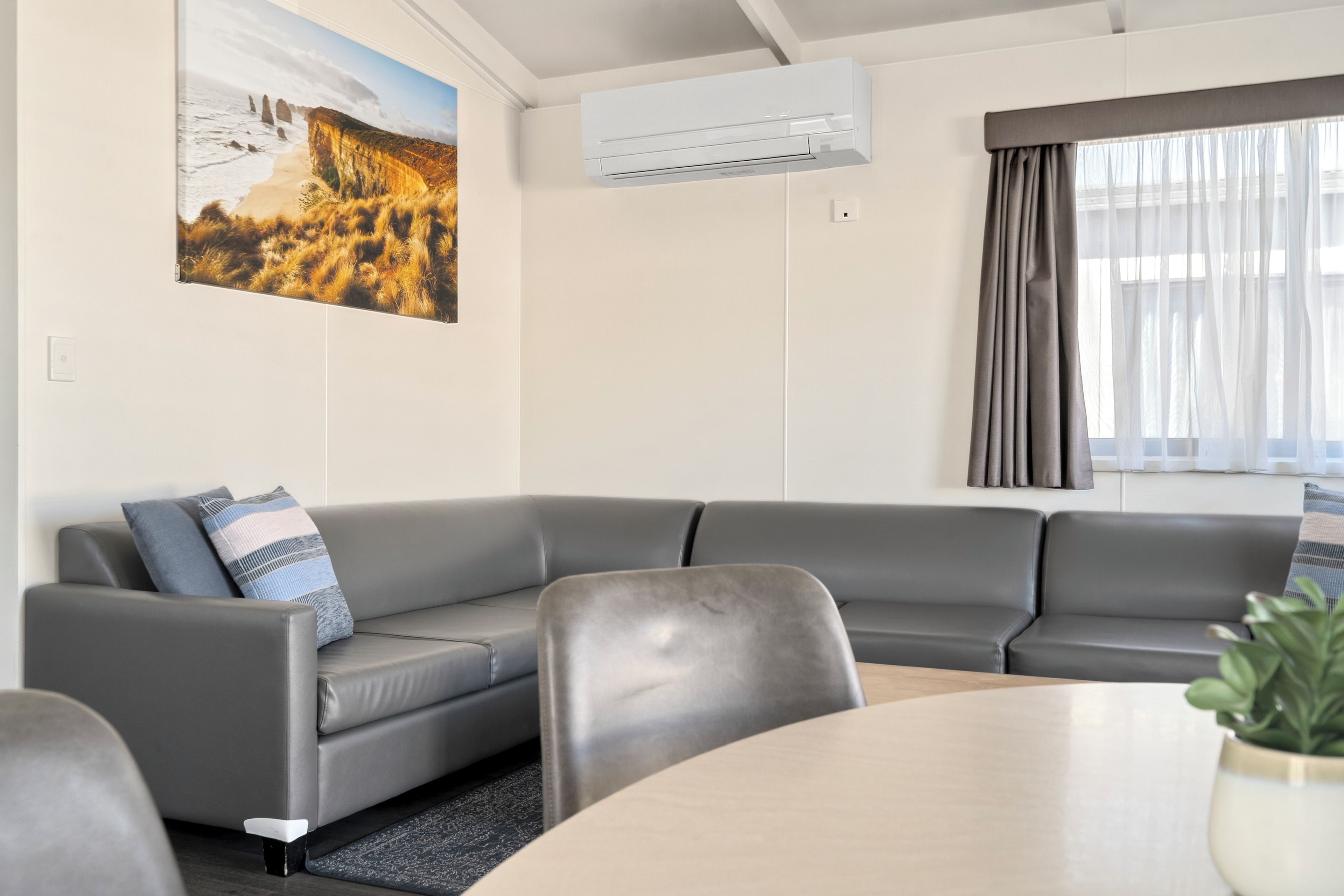 Una sala de estar moderna con un sofá de cuero gris, una mesa redonda y un amplio ventanal con cortinas.
