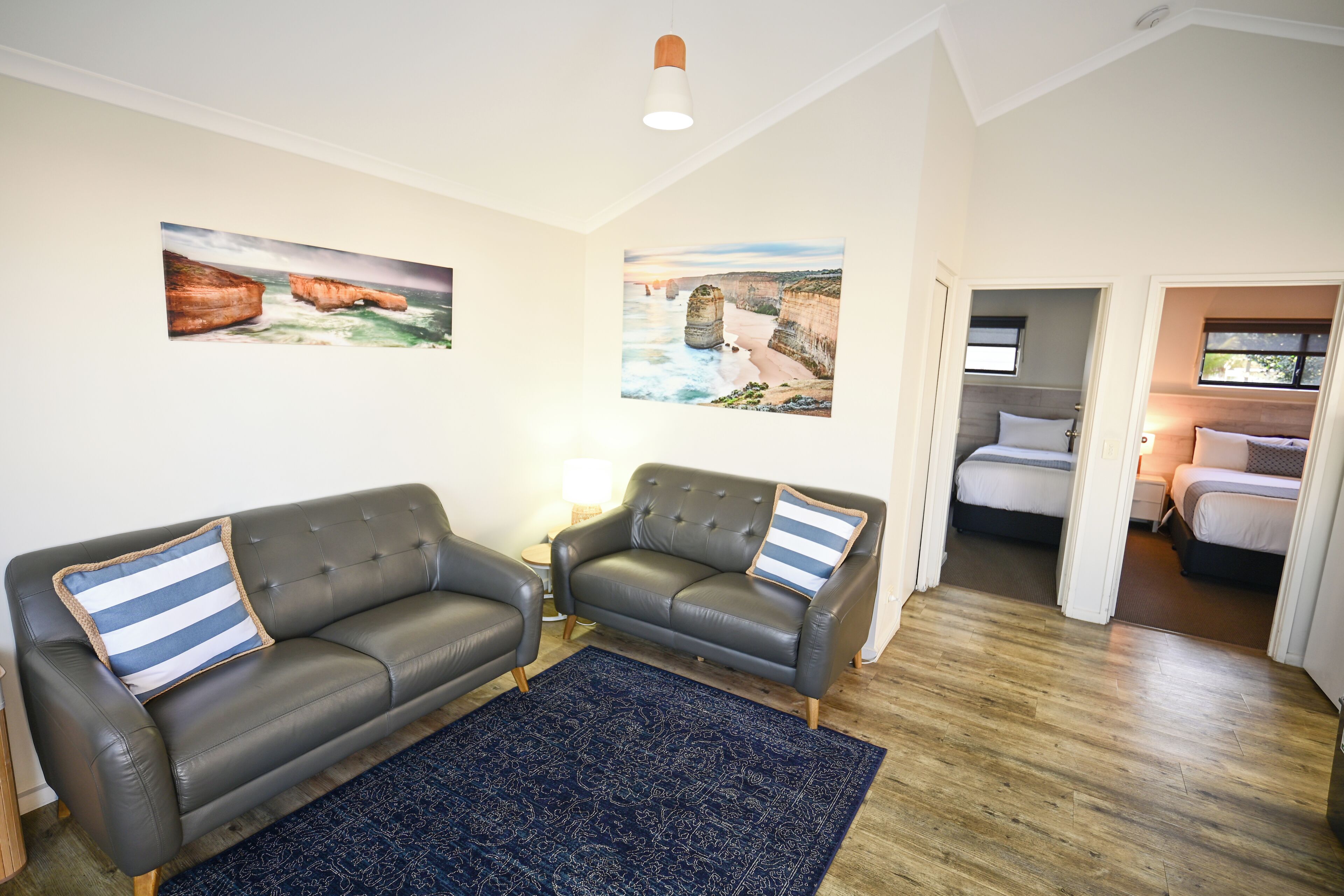 A room with two leather sofas, a blue patterned rug, and paintings of coastal landscapes on the walls.