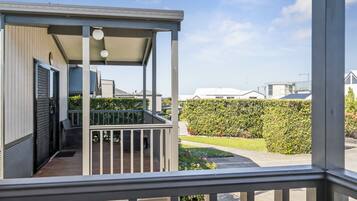 A covered outdoor area with a wooden deck, a metal railing, and a view of a neatly trimmed hedge and lawn.