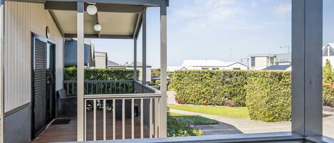 A covered outdoor area with a wooden deck, a metal railing, and a view of a neatly trimmed hedge and lawn.