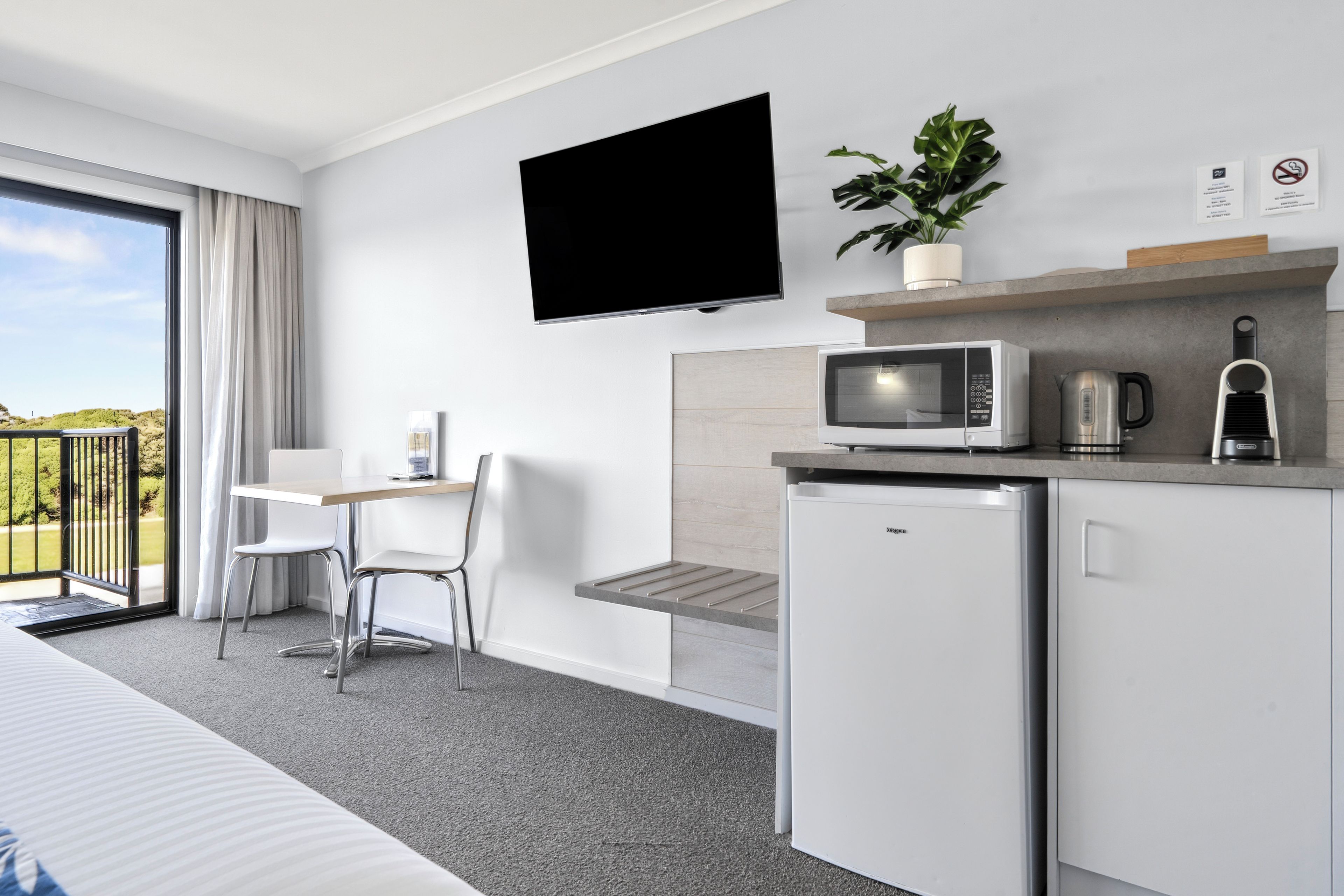 Habitación de hotel con cama, escritorio, silla, televisor, microondas, refrigerador y balcón con vistas.