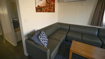 Een moderne woonkamer met een grijze modulaire bank, een decoratief kussen met een patroon, een houten salontafel en een schilderij van een kustlandschap aan de muur.