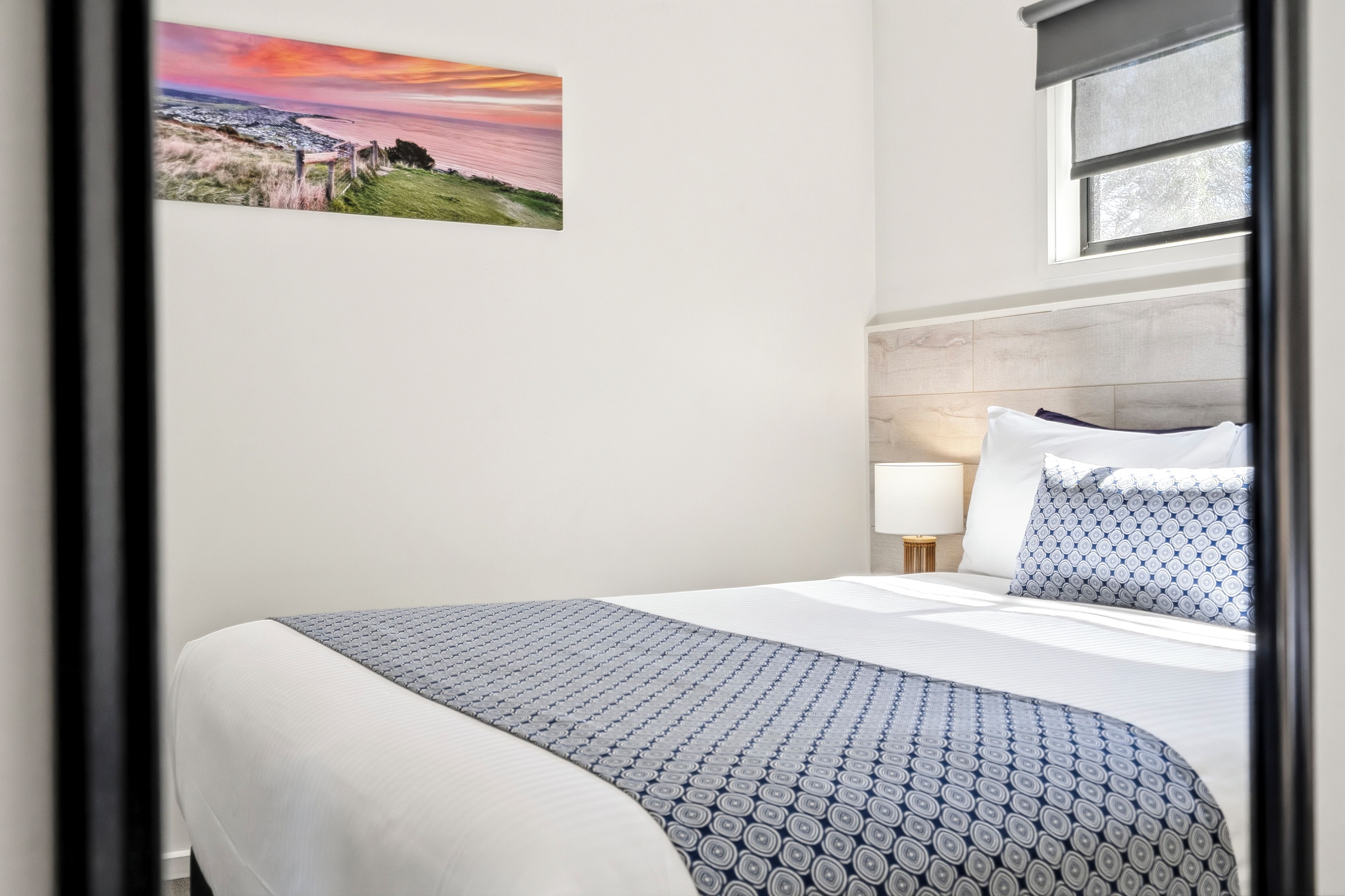 A hotel room with a bed, a nightstand, a lamp, and a window with a view of the sea.