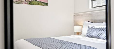 A hotel room with a bed, a nightstand, a lamp, and a window with a view of the sea.