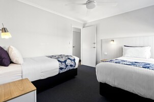 Habitación de hotel con dos camas, ventilador de techo y mesita de noche.