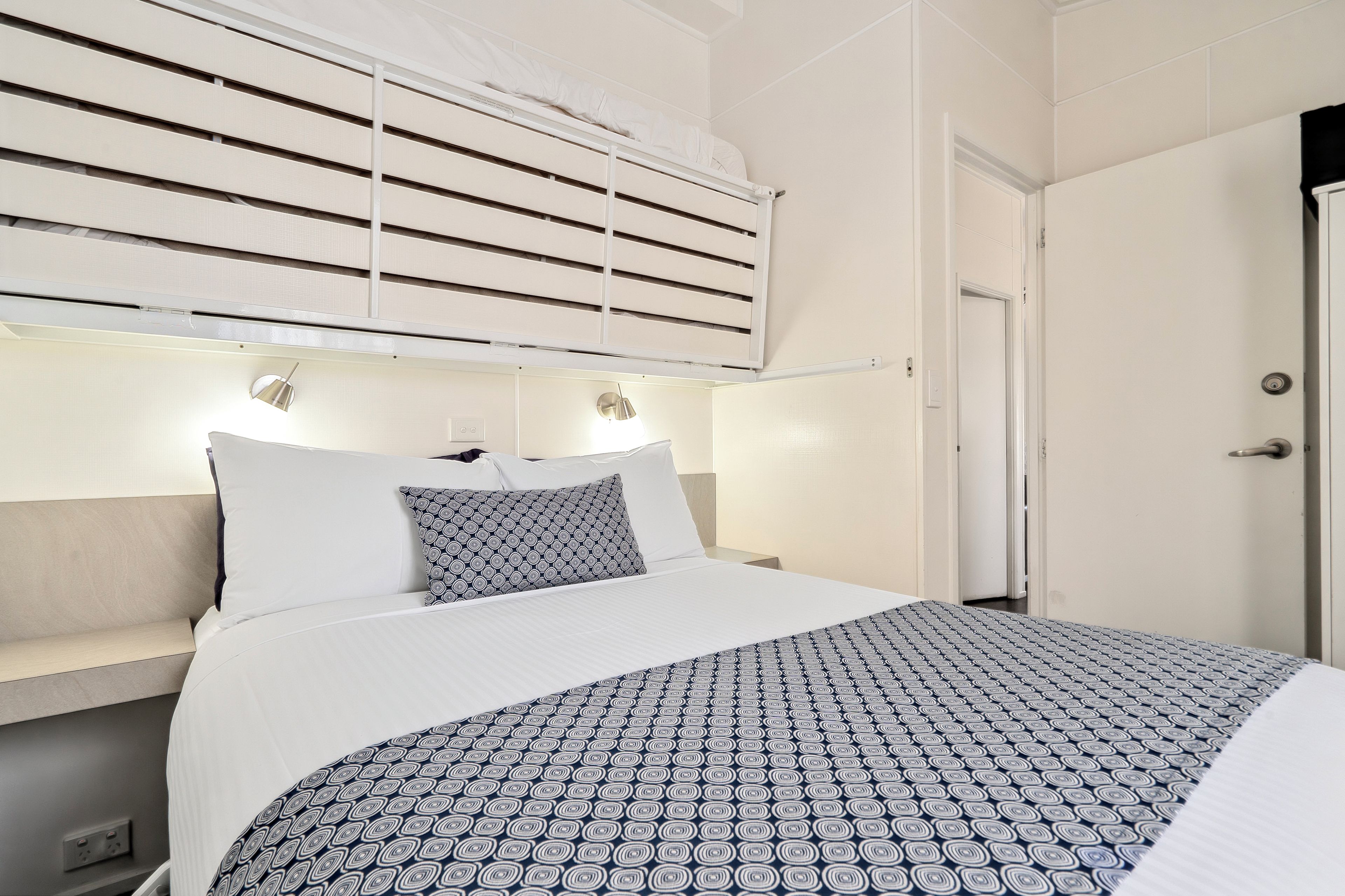 A hotel room with a bed, bedside lamps, a window with blinds, and a door.
