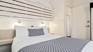 A hotel room with a bed, bedside lamps, a window with blinds, and a door.