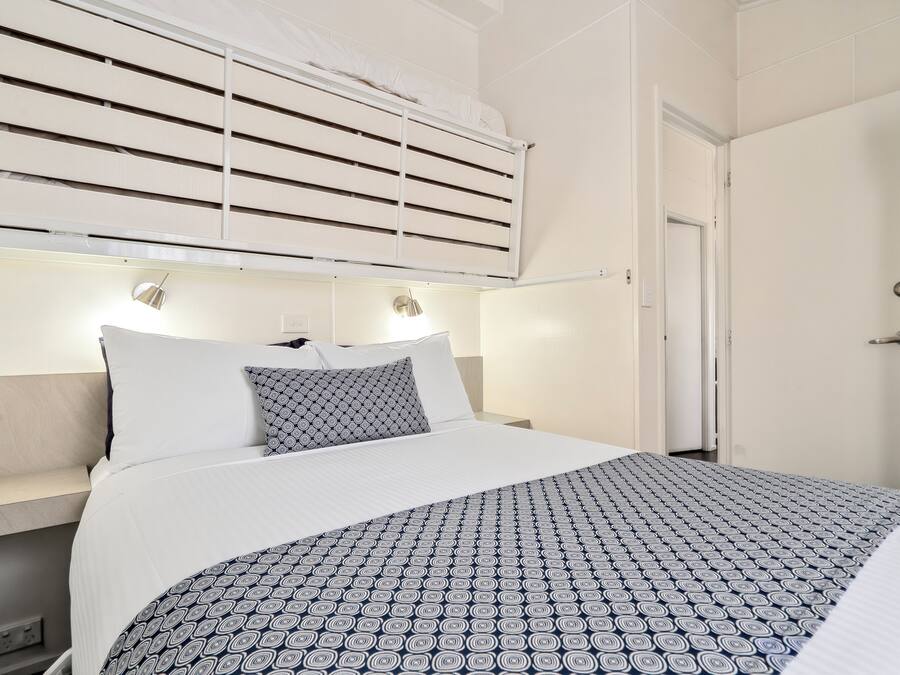 A hotel room with a bed, bedside lamps, a window with blinds, and a door.
