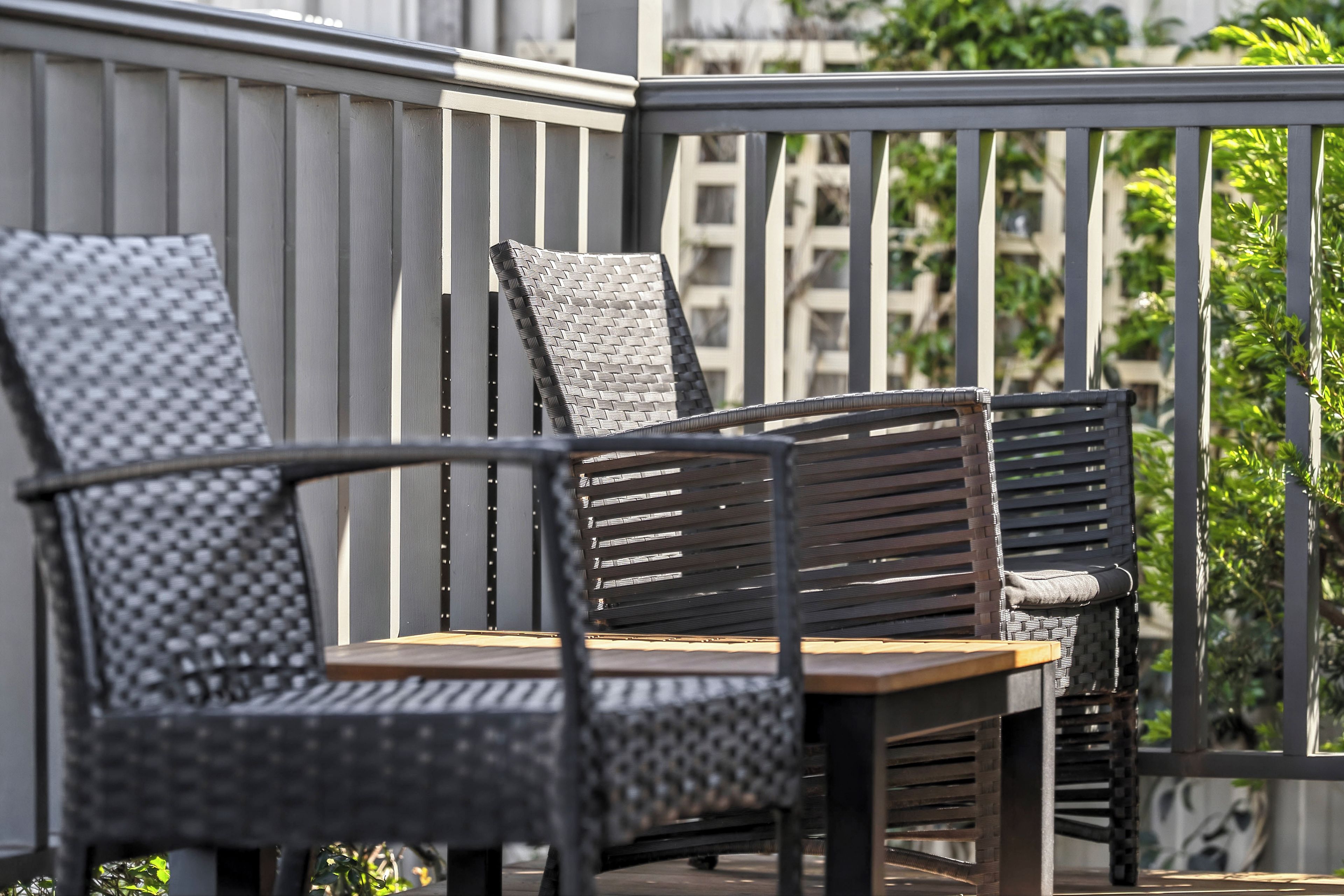 A balcony with two wicker chairs and a wooden table.