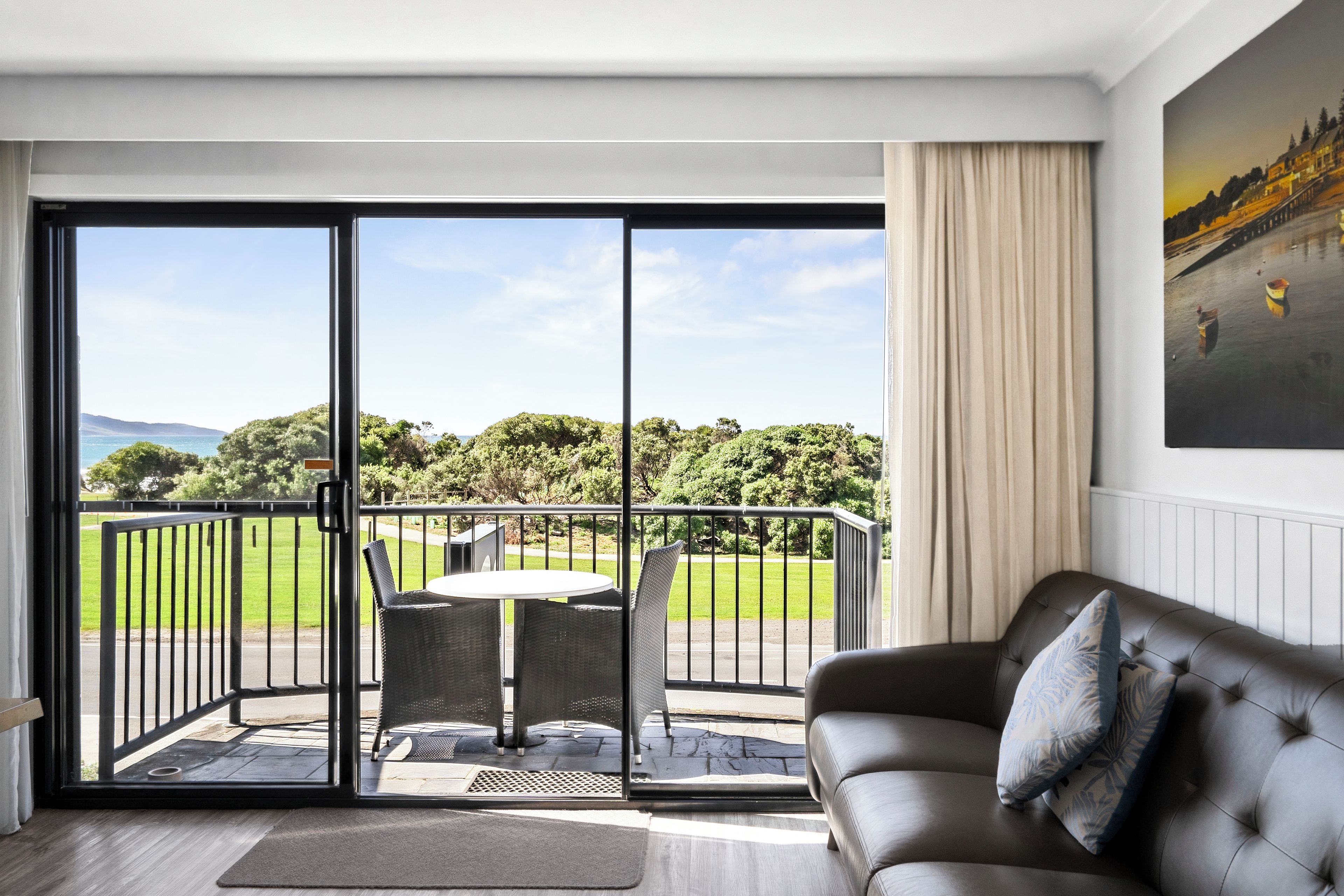 Ein modernes Wohnzimmer mit einer Couch und einem Tisch, ein Balkon mit Blick auf einen Golfplatz und ein Gemälde an der Wand.