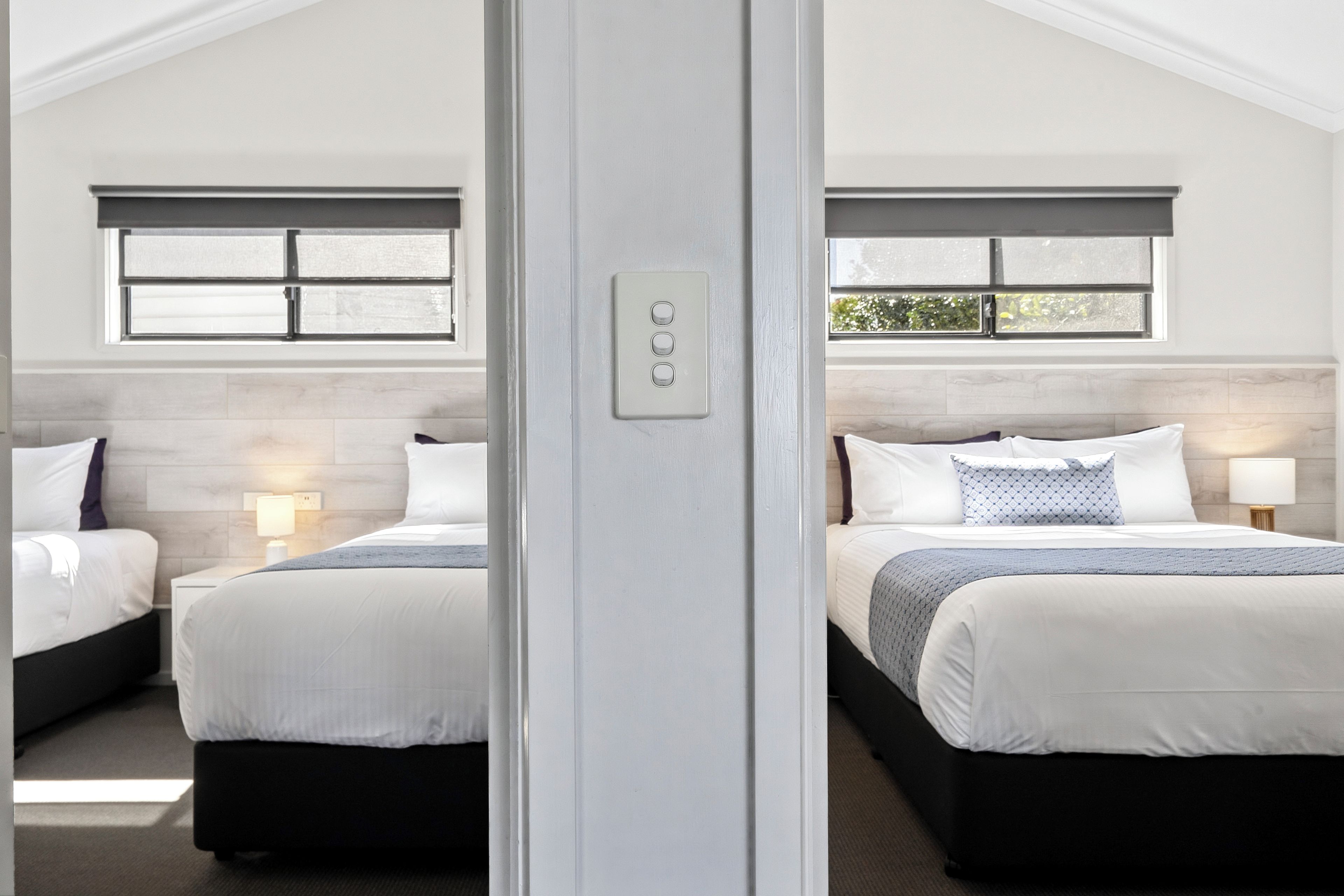Een hotelkamer met twee bedden, een raam en een lichtschakelaar aan de muur.