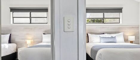 Een hotelkamer met twee bedden, een raam en een lichtschakelaar aan de muur.
