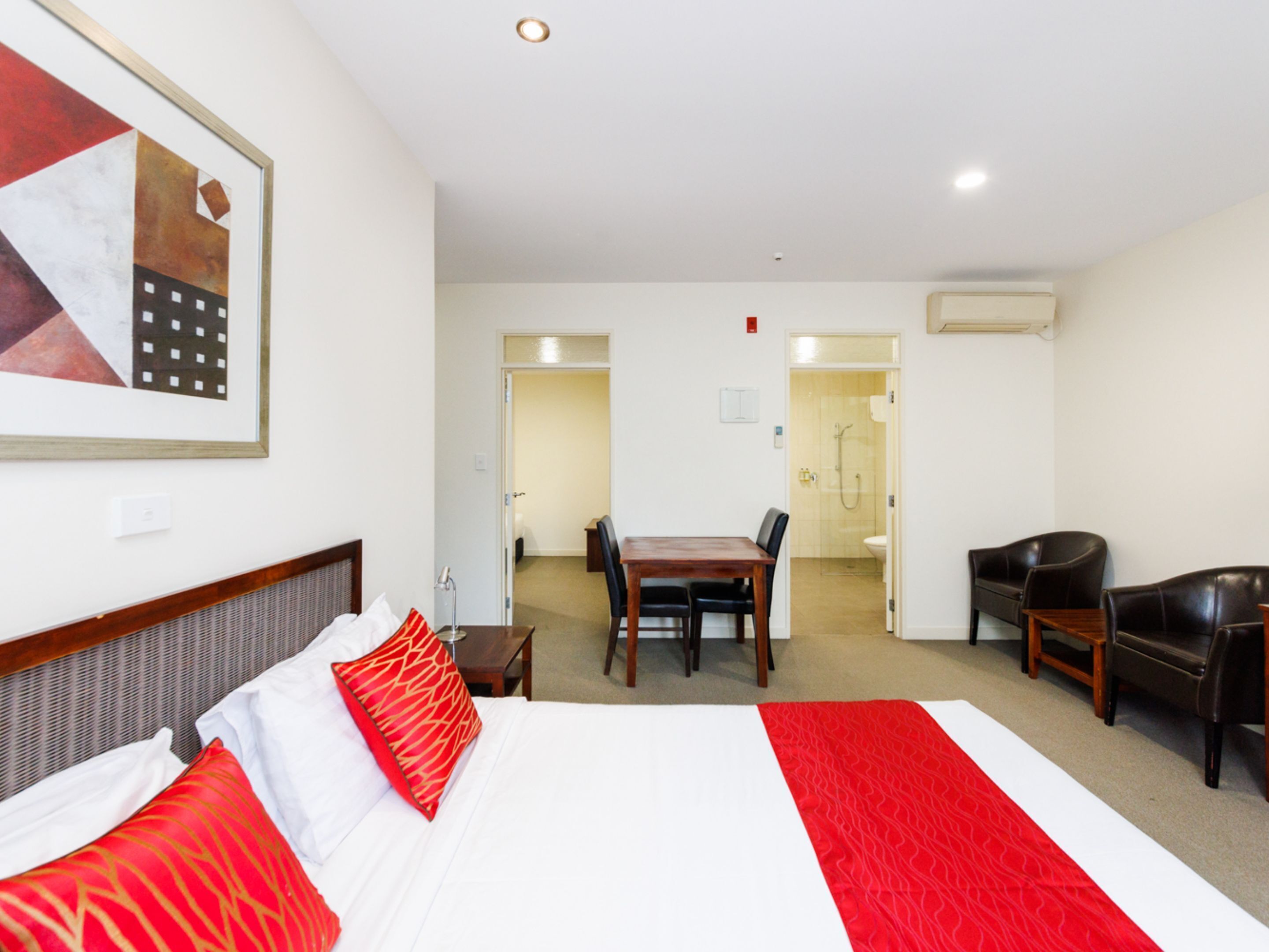 A hotel room with a large bed, a dining table, and a shower area.