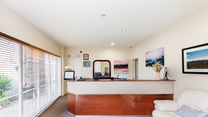 A reception area with a wooden counter, a mirror, framed certificates, and a painting. - Fitzherbert Regency Motor Lodge (Palmerston North)
