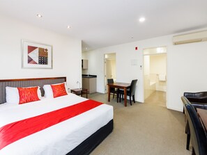 A hotel room with a large bed, a desk, and a chair. There is a kitchen area visible through an open door. - Fitzherbert Regency Motor Lodge (Palmerston North)