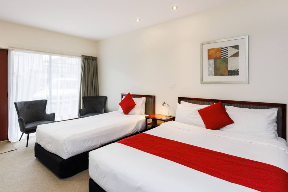 A hotel room with two beds, a desk, a chair, and a window with curtains.