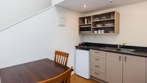A compact kitchen with a wooden dining table, white cabinets, and a built-in microwave shelf. - Fitzherbert Regency Motor Lodge (Palmerston North)