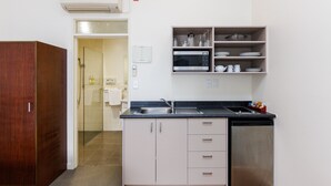 A compact kitchen with a microwave, sink, and a dishwasher. There is a wooden wardrobe and a small seating area with a red cushion. - Fitzherbert Regency Motor Lodge (Palmerston North)