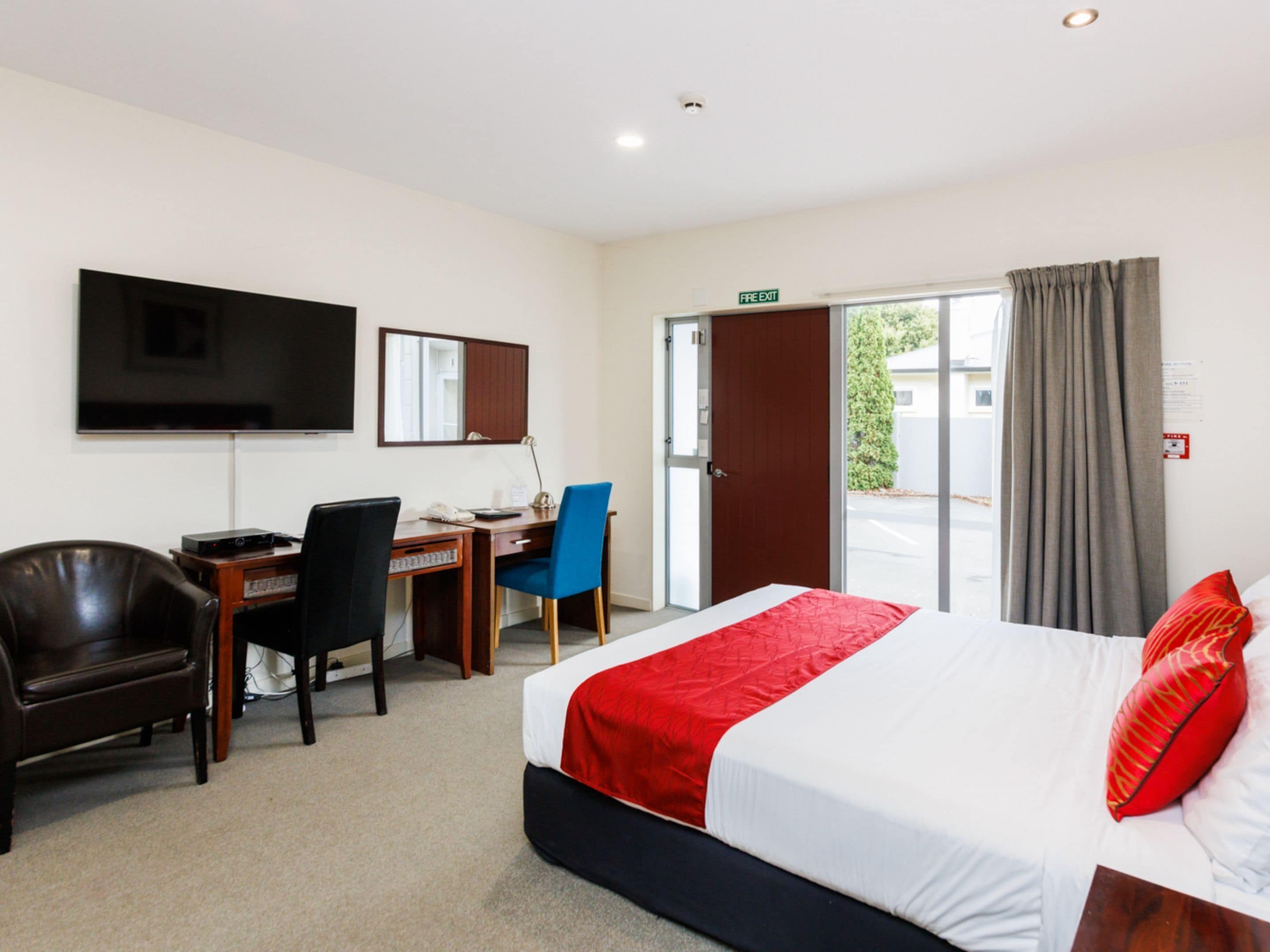 Een hotelkamer met een bed, een bureau, een stoel, een televisie en een deur naar buiten.