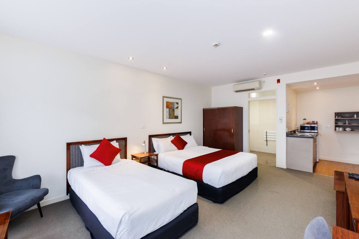 A hotel room with two beds, a desk, a chair, and a kitchenette.