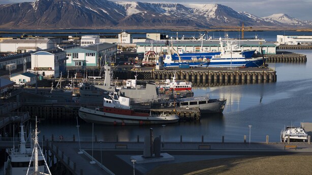 A harbor with boats docked, a pier, and a mountainous backdrop.