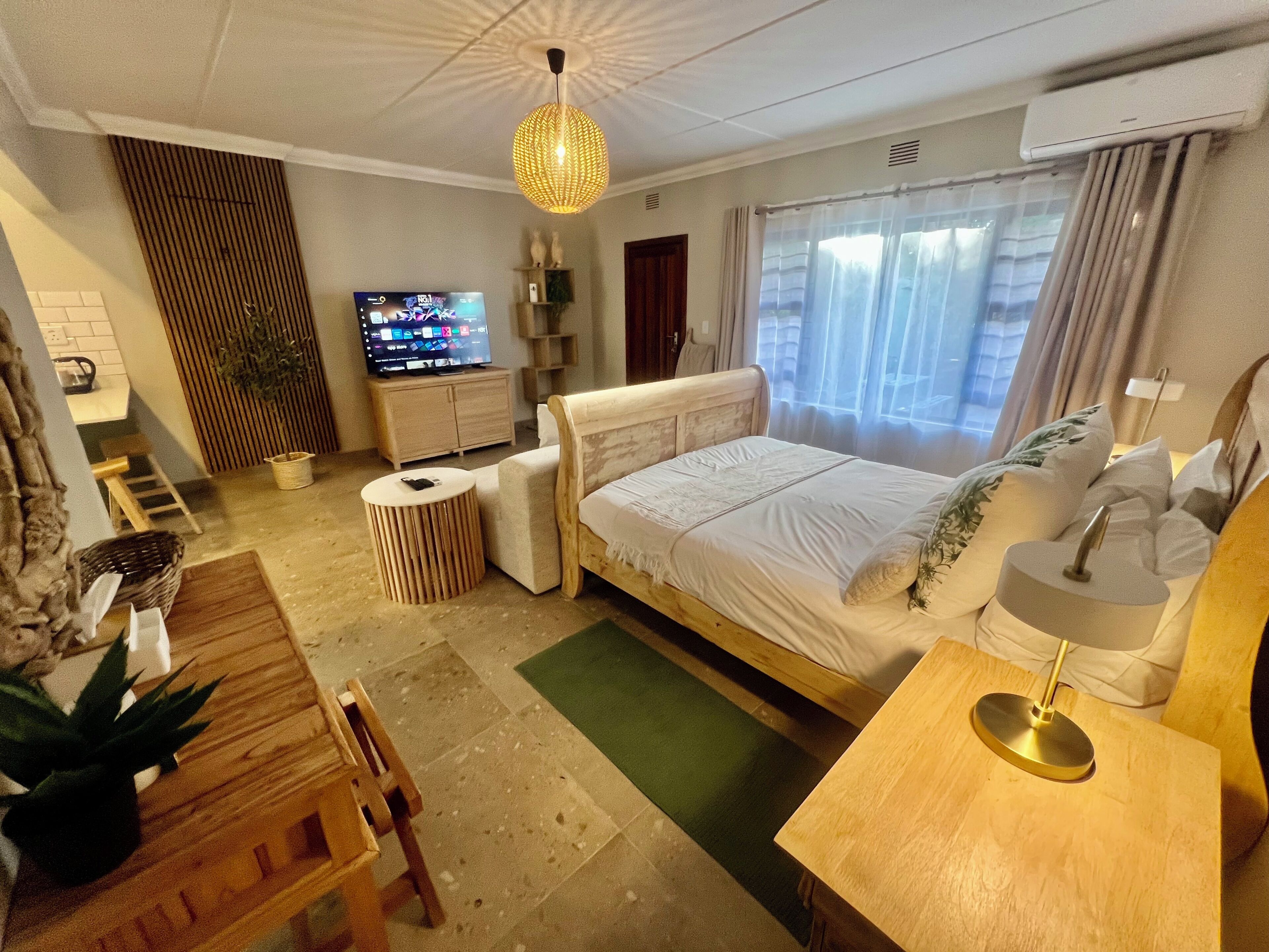 Ein Hotelzimmer mit Bett, Fernseher, Schreibtisch, Stuhl, Lampe und Pflanze.