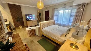 Ein Hotelzimmer mit Bett, Fernseher, Schreibtisch, Stuhl, Lampe und Pflanze.