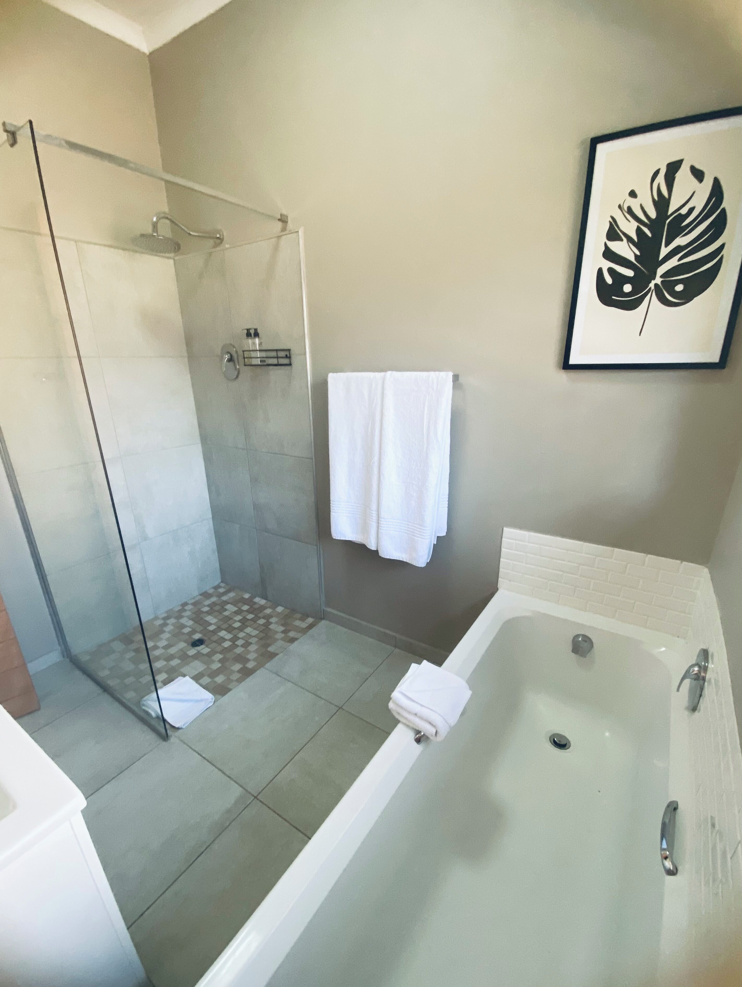 A modern bathroom with a glass-enclosed shower, a bathtub, and a framed artwork on the wall.