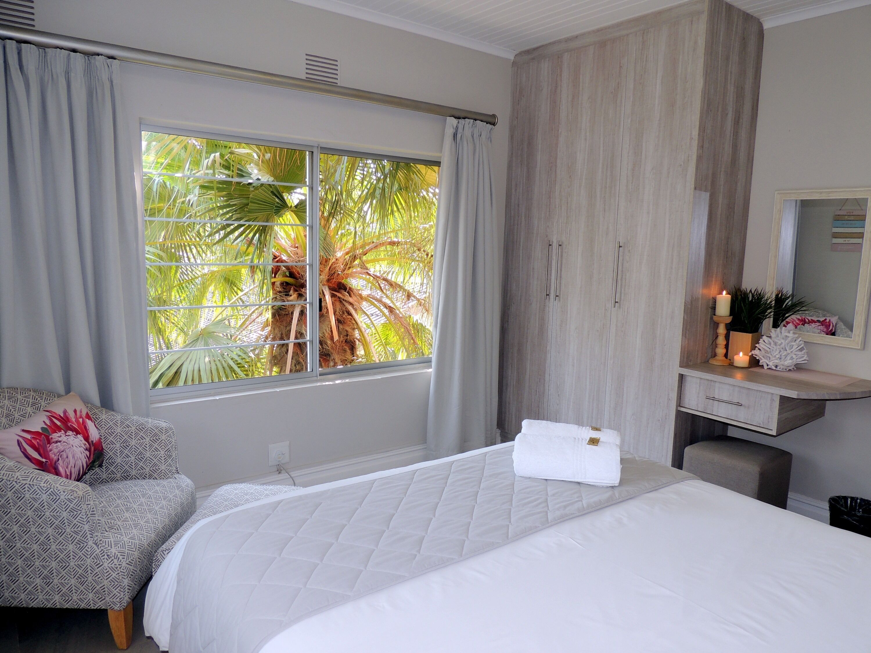 Um quarto com cama, mesa de cabeceira, cadeira, janela com cortinas e guarda-roupa.