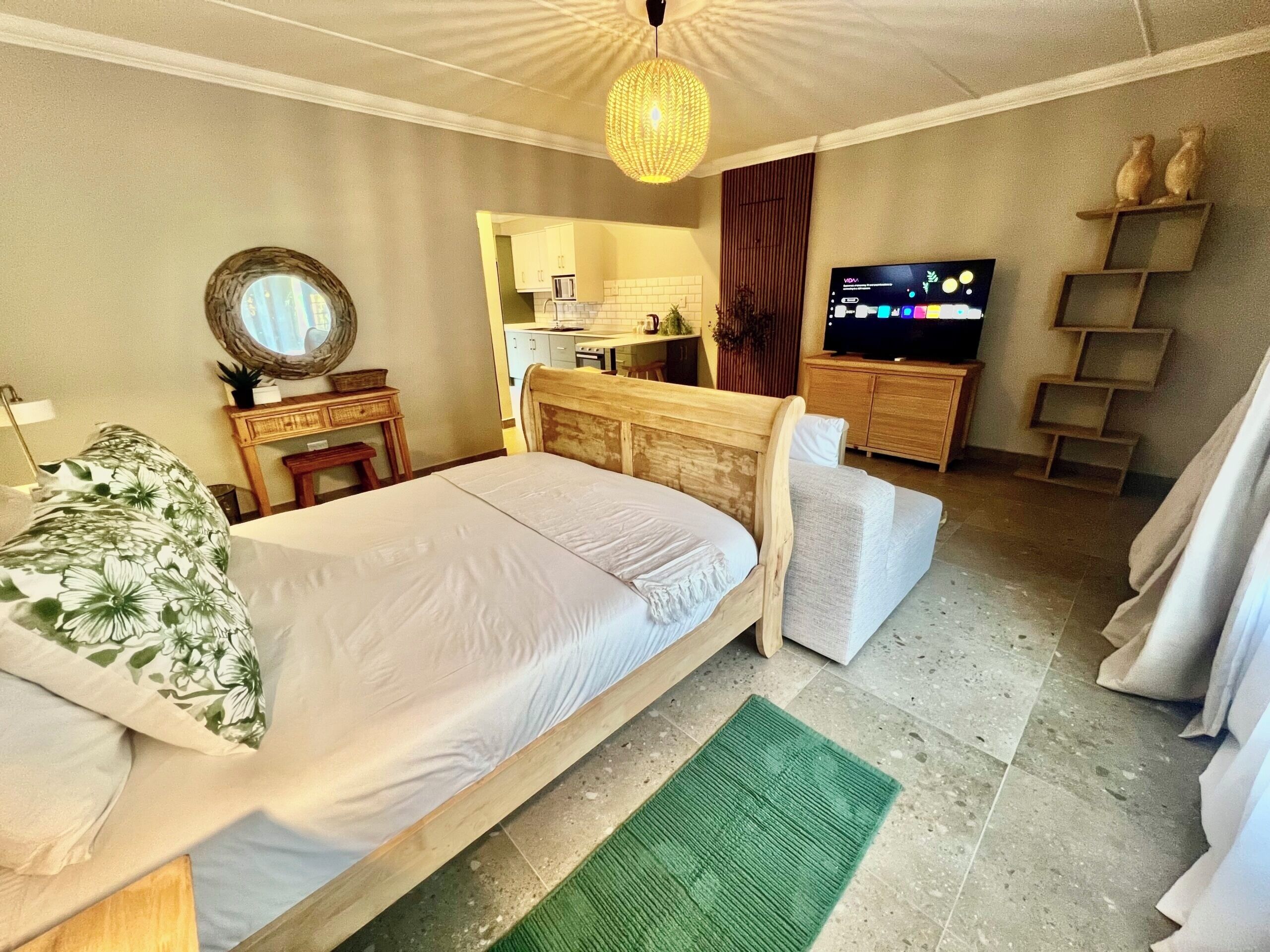 A bedroom with a bed, a television, a small kitchenette, and a bathroom visible through an open door.