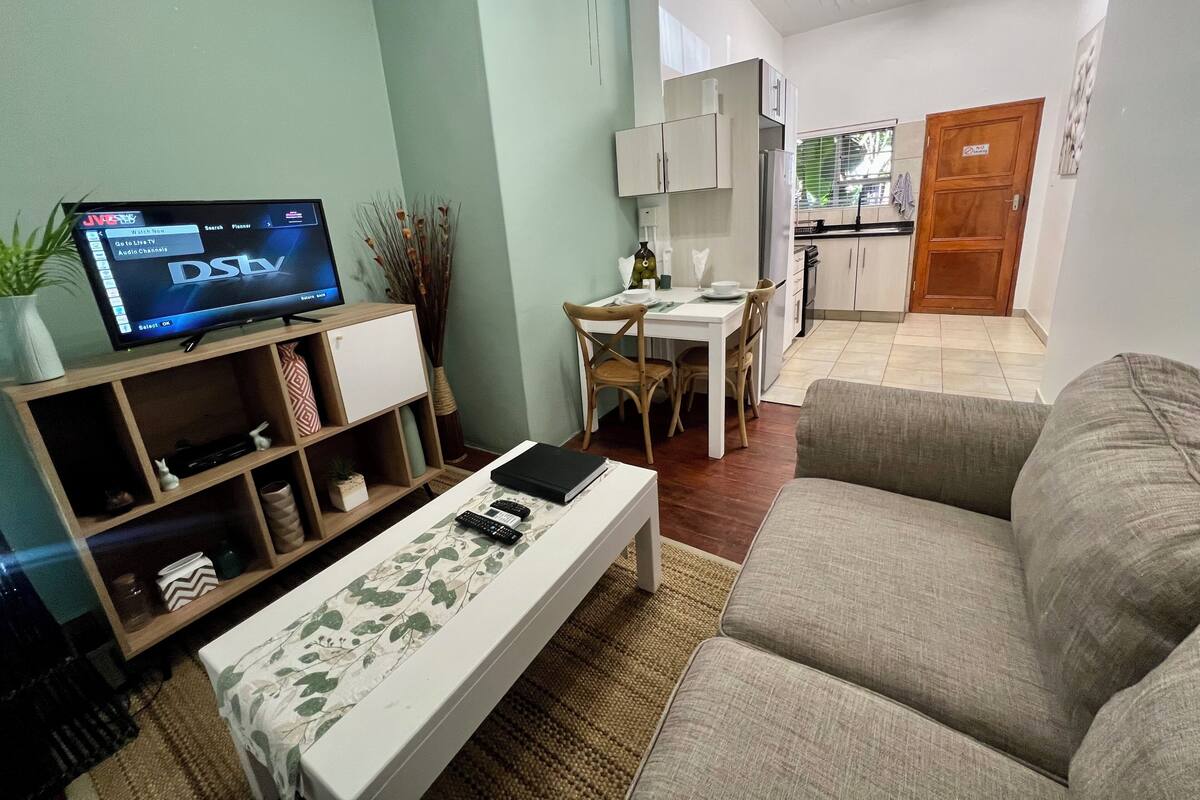 A living room with a flat-screen TV, a sofa, a coffee table, and a dining area with a table and chairs.