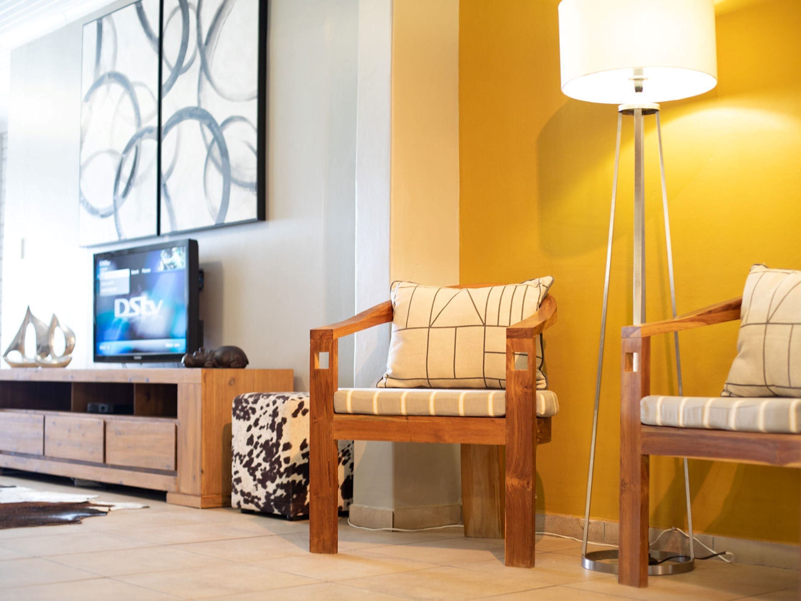 A living room with a wooden sofa, a patterned cushion, a television, and a floor lamp.