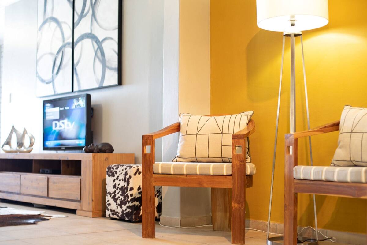 A living room with a wooden sofa, a patterned cushion, a television, and a floor lamp.