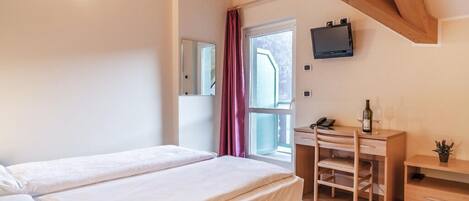 Un dormitorio con cama, escritorio, silla, televisor y ventana con cortinas.