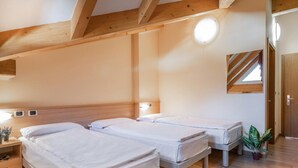 Un dormitorio con dos camas individuales, vigas de madera, una mesita de noche con lámpara, una planta en maceta y un espejo en la pared.