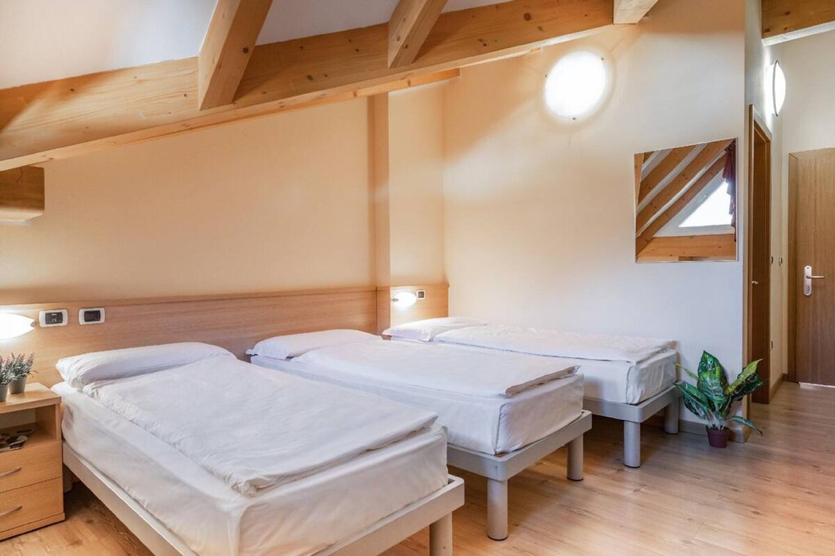 A bedroom with two single beds, wooden beams, a small bedside table with a lamp, a potted plant, and a mirror on the wall.