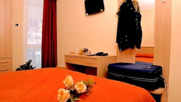 Camera d'albergo con un letto, una scrivania, una sedia, una valigia e un cappotto appeso al muro.
