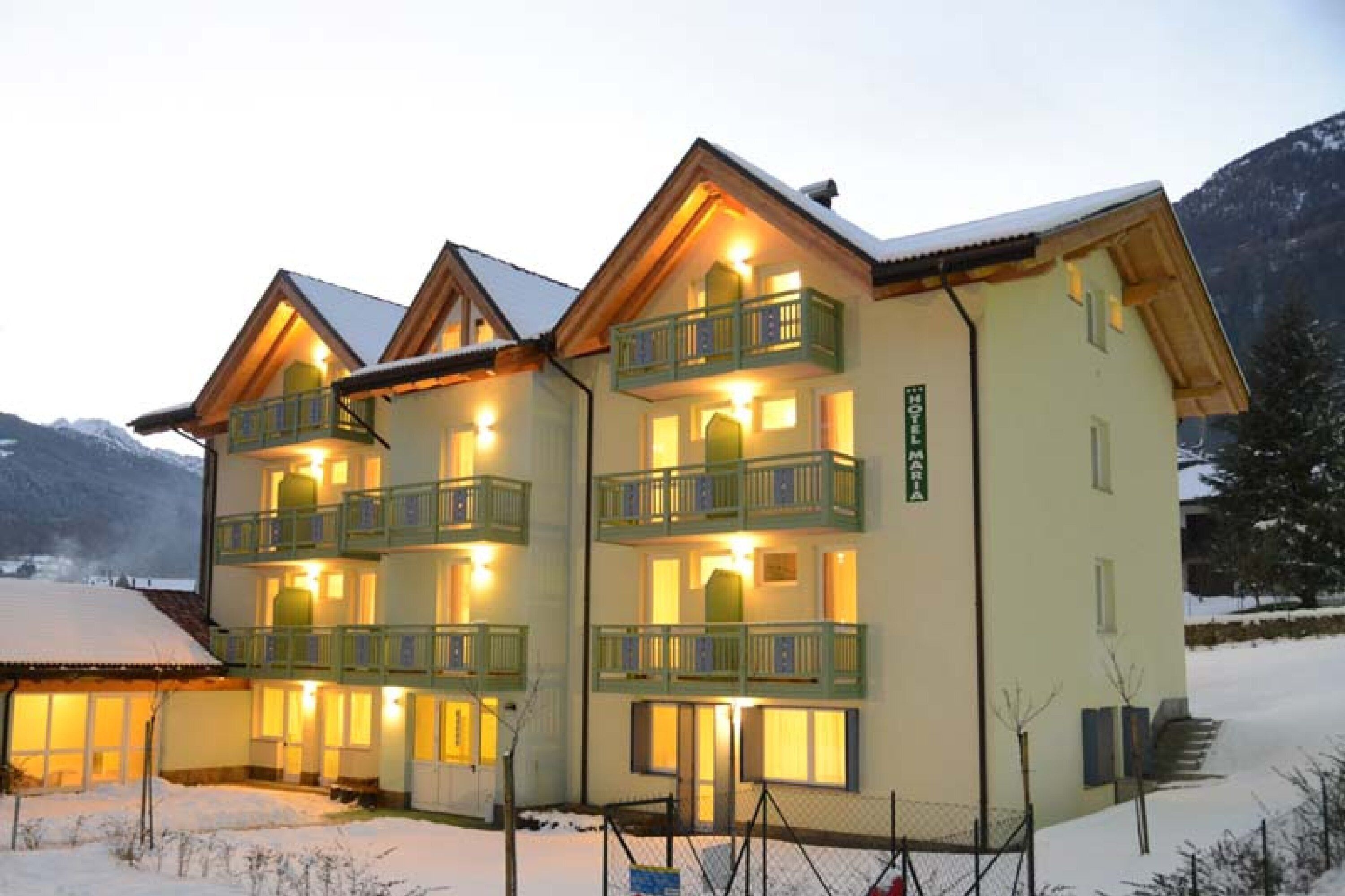 Un hotel de varios pisos con balcones, un paisaje cubierto de nieve y montañas al fondo.