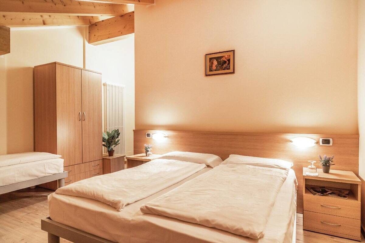 A bedroom with two beds, wooden wardrobe, bedside tables with lamps, and a small wall-mounted picture.