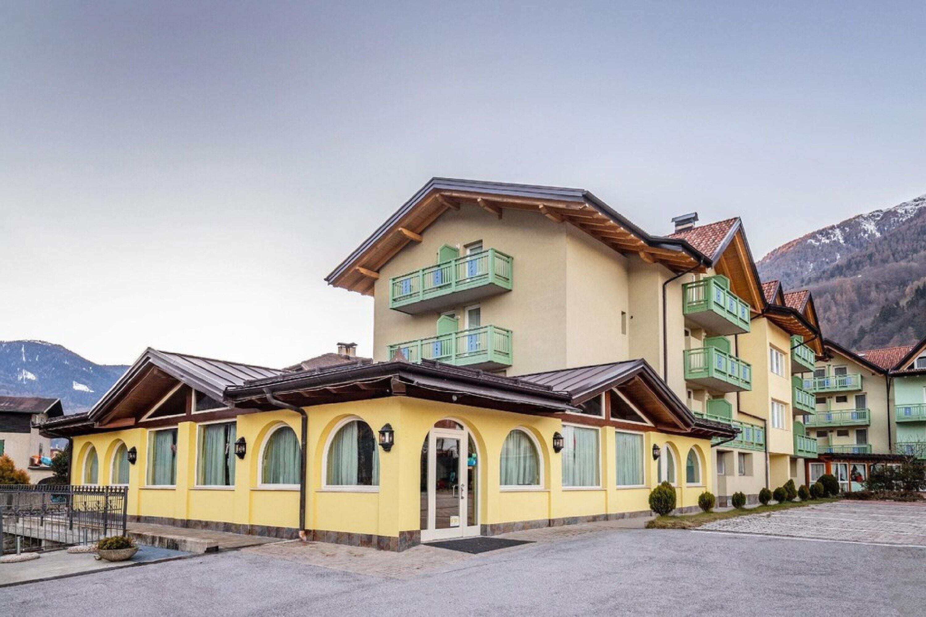 A yellow building with a balcony and arched windows, surrounded by mountains.