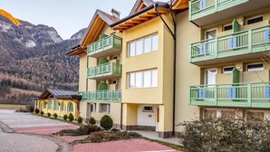 Un hotel de varios pisos con balcones, un estacionamiento y montañas al fondo.
