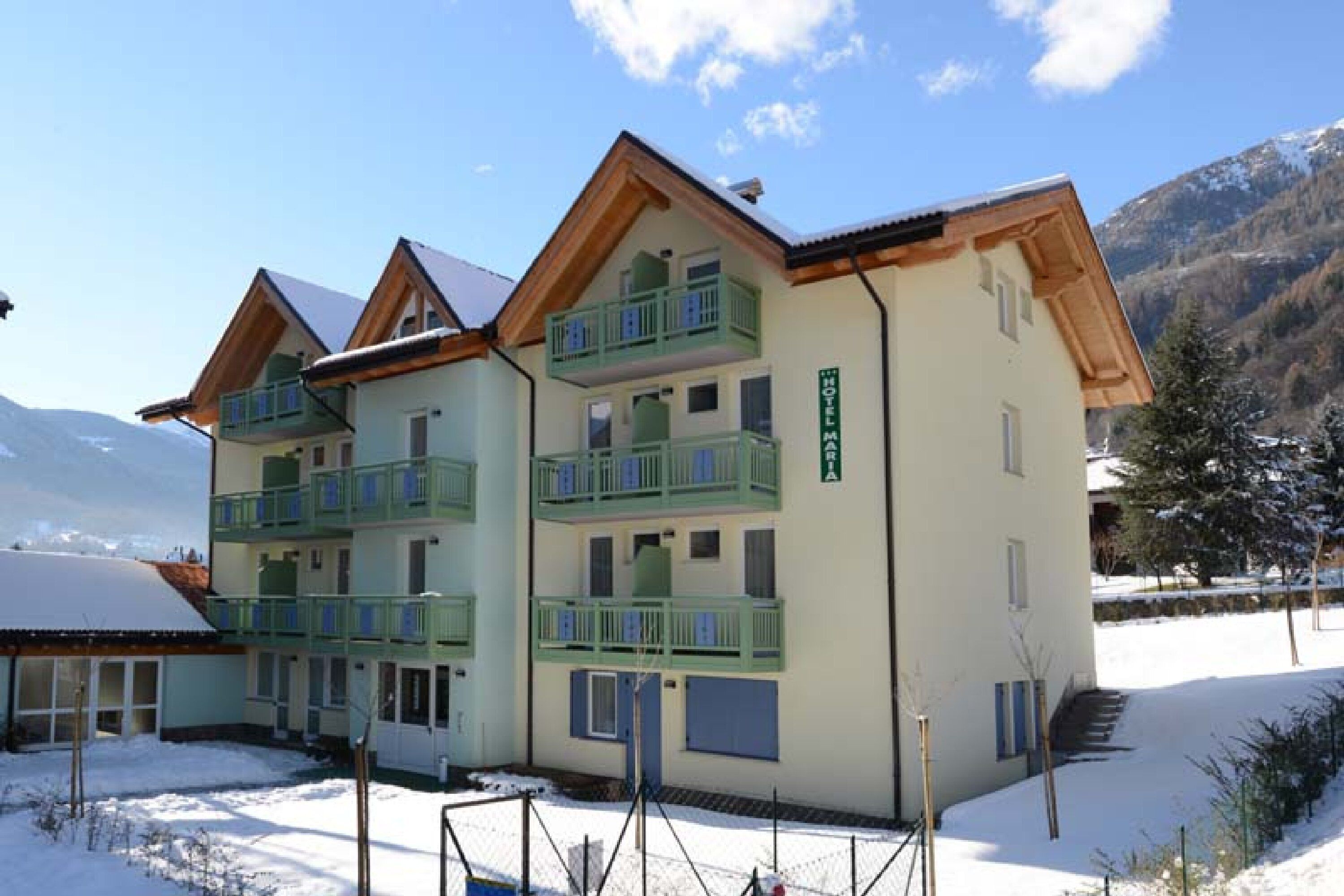 A multi-story hotel with balconies, a ski slope in the background, and a mountainous landscape.