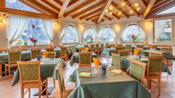 Un restaurante con vigas de madera y ventanas amplias, mesas dispuestas con manteles verdes y sillas.