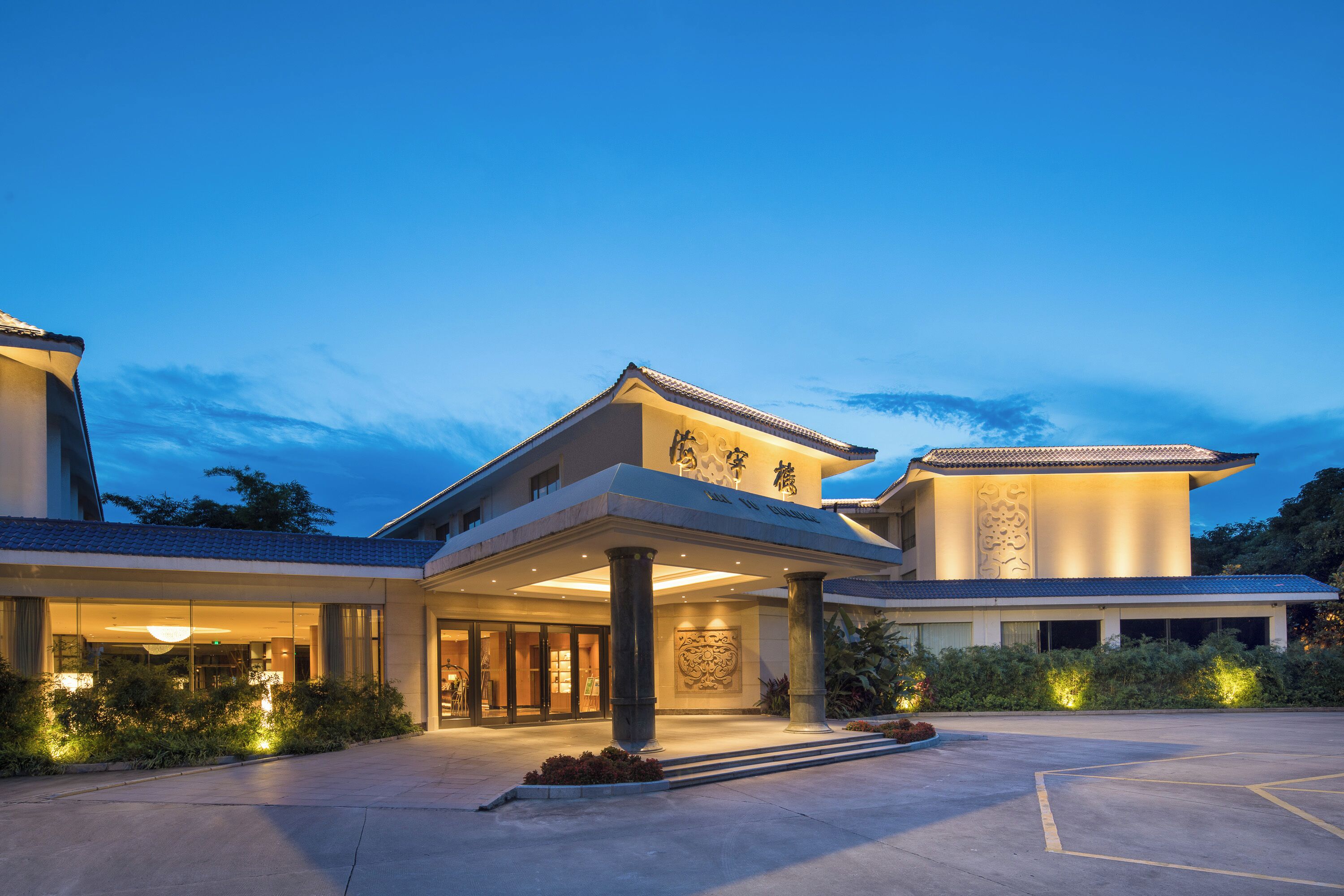 A hotel with a traditional architectural style, featuring a prominent entrance with a covered walkway, large columns, and a well-lit facade.