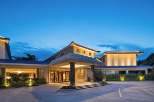 A hotel with a traditional architectural style, featuring a prominent entrance with a covered walkway, large columns, and a well-lit facade.